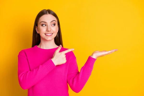 Фото очаровательной леди прямой палец держать руку смотреть пустое пространство носить розовый свитер изолированный желтый цвет фона — стоковое фото