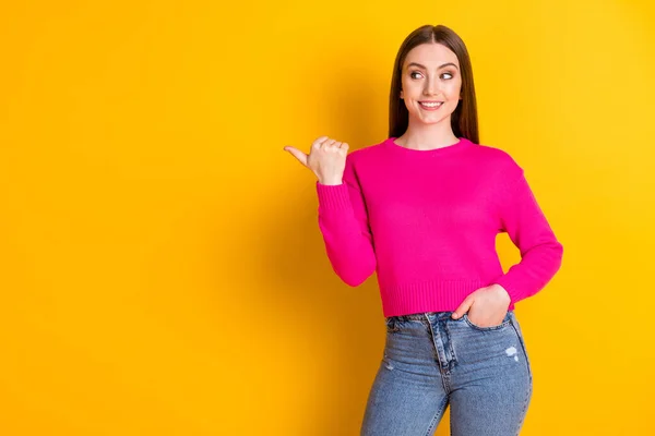 Foto de chica encantadora mirada pulgar directo espacio vacío bolsillo de mano desgaste pantalones vaqueros suéter rosa aislado color amarillo fondo — Foto de Stock