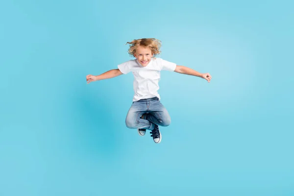 Фото маленького дитячого стрибка смішний вигляд фотоапарата піднімають руки в білій сорочці джинси кросівки ізольовані синій колір фону — стокове фото
