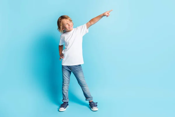 Фотографія маленької дитини, що піднімає руку, вказує на те, що палець виглядає порожнім простором у білій сорочці джинси кросівки ізольовані синій колір фону — стокове фото