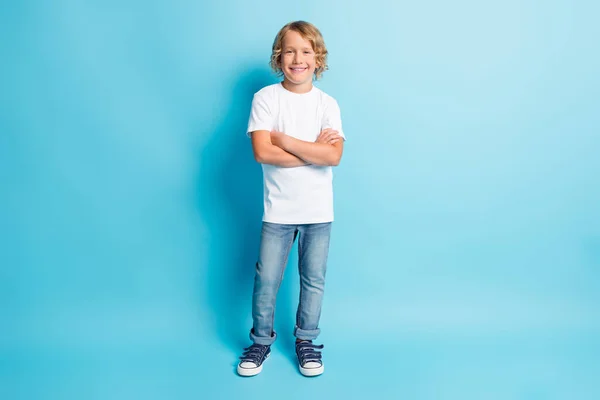 Foto de comprimento total de criança cruzou os braços ondulado penteado olhar câmera desgaste jeans branco camisa tênis isolado azul cor fundo — Fotografia de Stock