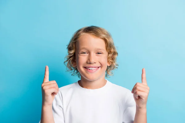 Foto de menino indicador de ponto dedo para cima copyspace para publicidade promoção desgaste t-shirt branca isolada no fundo de cor azul — Fotografia de Stock