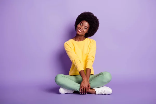 Teljes méretű fotó afro amerikai lány ül padló lábak keresztbe jó hangulatú mosoly elszigetelt lila szín háttér — Stock Fotó