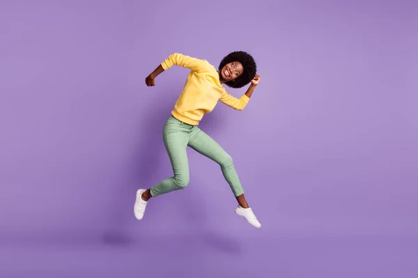 Foto de tamaño completo de la niña excitada piel oscura salto mueca desgaste jersey amarillo aislado sobre fondo de color púrpura — Foto de Stock