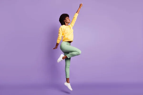Volledige lengte foto van krachtige donkere huid meisje springen raise vuisten vooruit dragen pullover broek geïsoleerd over paarse kleur achtergrond — Stockfoto
