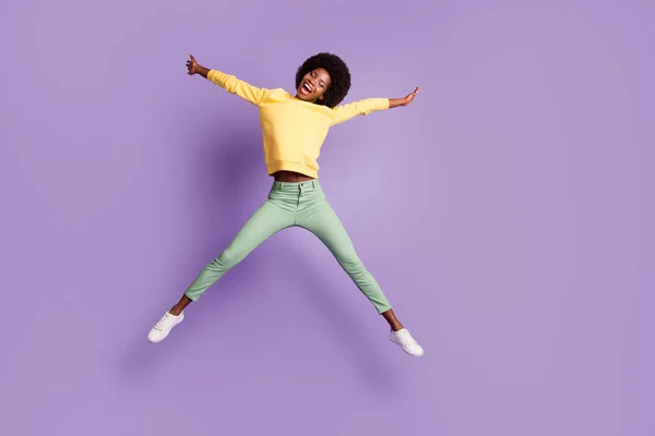 Foto de cuerpo completo de la niña afroamericana despreocupada salto usar suéter amarillo pantalones verdes aislados sobre fondo de color violeta —  Fotos de Stock