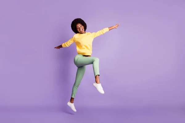 Foto em tamanho completo da menina pele escura animado saltar para cima desgaste amarelo suéter verde calças isoladas no fundo de cor roxa — Fotografia de Stock