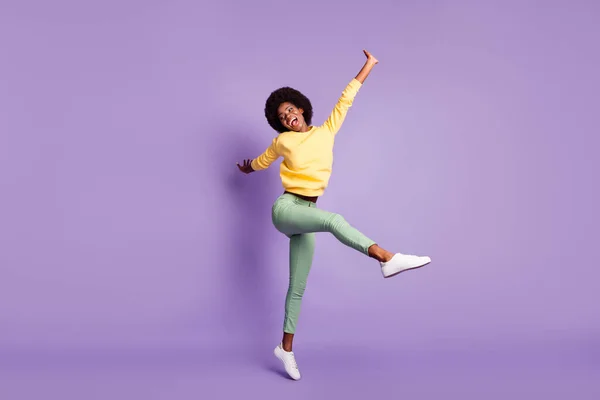 Volledige lengte foto van opgewonden afro-Amerikaanse meisje springen dragen gele pullover groene broek geïsoleerd op violette kleur achtergrond — Stockfoto