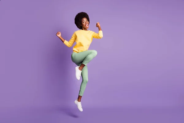미국 여자가 점프하는 모습의 전체 길이 사진 주먹질을 하고 있는 주먹질을 하고 있는 보라색 배경 위에 따로 떨어져 있는 노란 풀무를 착용하고 있다 — 스톡 사진
