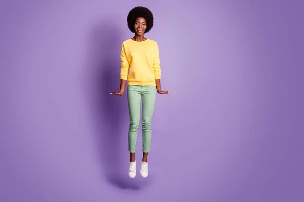 Foto de tamaño completo de despreocupado niña afro americana alegre saltar usar pantalones de suéter verde amarillo aislado sobre fondo de color púrpura — Foto de Stock