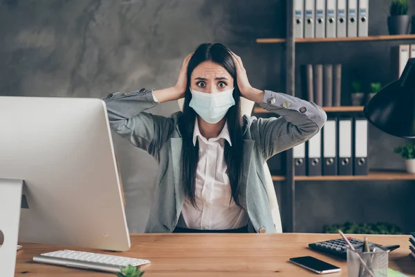 Photo of shocked worried girl medical mask agent representative sit desk table hear boss horrible news company bankrupt she will lose job panic touch hands head in workplace workstation