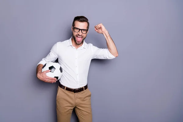 Фото симпатичного взволнованного парня с бородой, смотрящего футбол, держащего в руках спортивный мяч, поддерживающего команду, изолированную на фоне серого коллора — стоковое фото