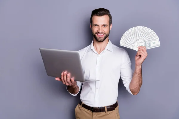 Portret van zijn hij mooie aantrekkelijke rijke succesvolle vrolijke brunet kerel met behulp van laptop holding in handen investering spelen online casino spel inzet geïsoleerd over grijs pastel kleur achtergrond — Stockfoto