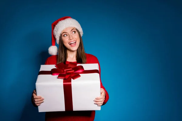 Fényképezés positive girl in santa claus cap look copyspace hold dream big white gift box enjoy magic Karácsony x-mas esemény viselni kötött pulóver jumper elszigetelt sötét kék háttér — Stock Fotó