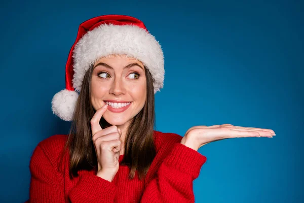 Фотографія позитивної дівчини в капелюсі Санта Клауса тримає руку демонструє X-mas newyear рекламний сенсорний палець зуби носити теплий зимовий сезон одяг ізольований синій градієнтний кольоровий фон — стокове фото