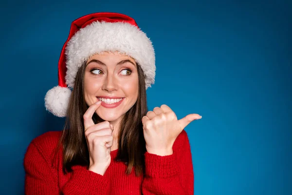 Foto pozitivní dívka v Santa Claus klobouk dotykový prst zuby bod ukazováček copyspace sen vzhled x-mas víla cesmína inzeráty propagace nosit svetr svetr izolované modré barvy pozadí — Stock fotografie