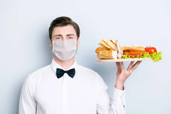 Közelkép portré egy előkelő fickó pincér visel biztonsági maszk tartó tálca finom ételek elszigetelt szürke színű háttér — Stock Fotó
