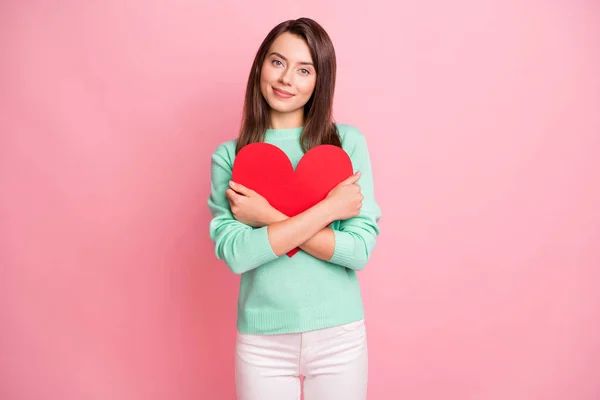 Retrato de menina calma alegre atraente segurando em mãos abraçando coração de papel vermelho isolado sobre fundo de cor pastel rosa — Fotografia de Stock