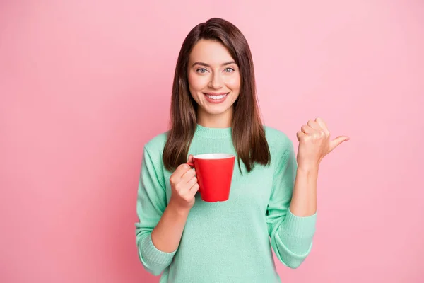 Fotografie veselé hezká brunetka rovné vlasy dívka držet pohár bod prázdný prostor oblečení svetr izolované na růžové pozadí — Stock fotografie