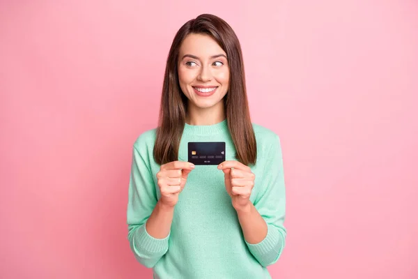 Photo of cute funny brunette girl stand show debit card look empty space wear pastel sweater isolated on pink color background — Stock Photo, Image