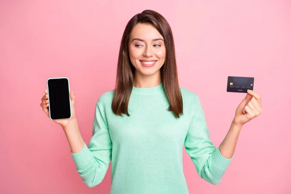 Foto av dam hålla telefon titta skärmen tomt utrymme kreditkort toothy leende bära turkos tröja isolerad rosa färg bakgrund — Stockfoto