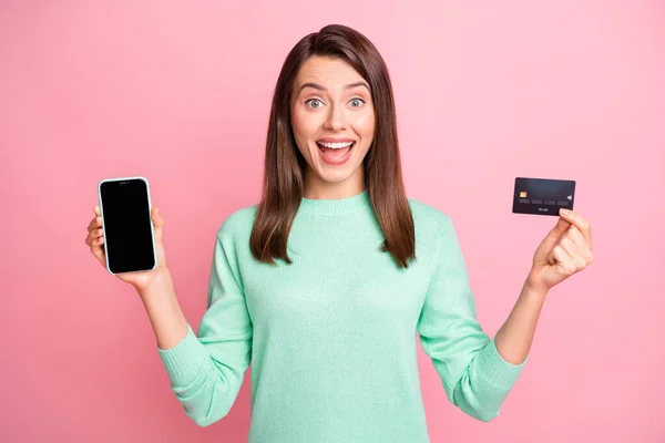 Foto de chica divertida pantalla del teléfono del asimiento espacio vacío tarjeta de crédito boca abierta desgaste jersey de color rosa aislado fondo —  Fotos de Stock