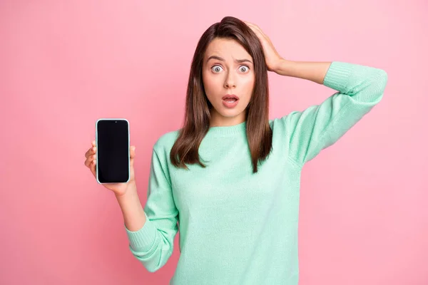 Fénykép a megdöbbent hölgy tartsa telefon képernyő üres tér kéz fej kopás rózsaszín pulóver elszigetelt rózsaszín háttér — Stock Fotó