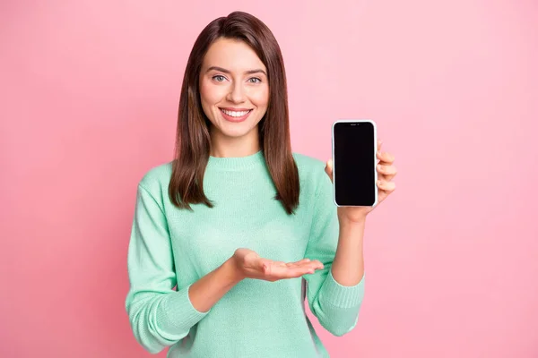 Foto av ganska ung flicka arm hålla telefon skärm tomt utrymme bära turkos pullover isolerad rosa färg bakgrund — Stockfoto