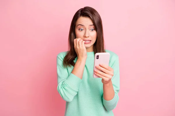 Foto van nerveuze meisje houden mobiele telefoon knagen nagels look scherm slijtage turquoise pullover geïsoleerde roze kleur achtergrond — Stockfoto