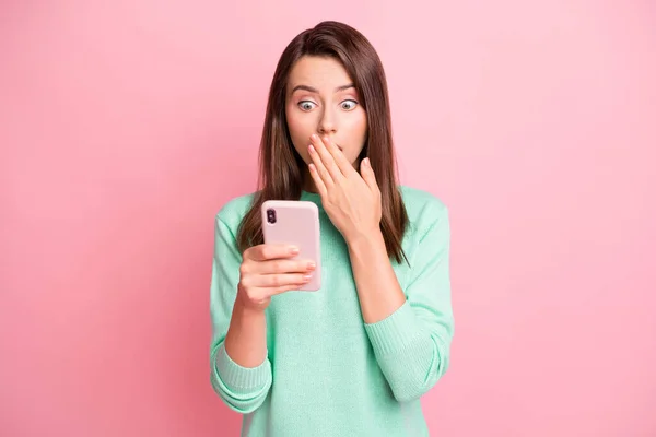Foto de chica sin palabras sostener teléfono inteligente mano cerrar la boca mirar pantalla usar jersey verde azulado aislado color rosa fondo — Foto de Stock