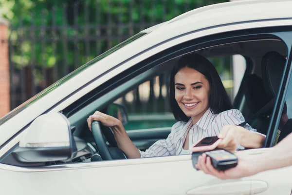 Foto av positiv flicka rida köra bil håll ratt betala inträde parkeringsplats smartphone pos terminal i centrum — Stockfoto