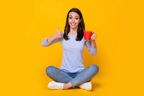 Retrato dela ela agradável atraente muito alegre alegre menina sentada posição de lótus beber cafeína mostrando polegar isolado brilhante brilhante brilho vibrante cor amarela fundo — Fotografia de Stock