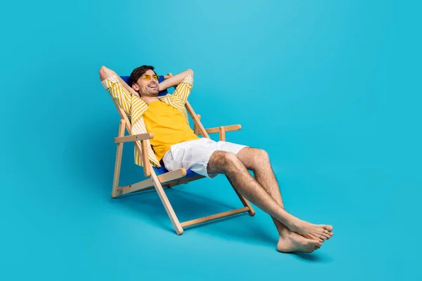 Foto lateral de perfil de longitud completa de viajero chico positivo relajarse descanso playa tomar el sol mentira comodidad tumbona manos elásticas usar pantalones cortos blancos aislados sobre fondo de color azul —  Fotos de Stock