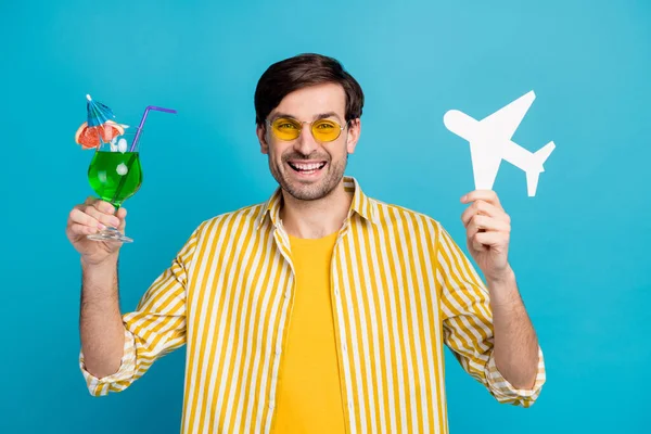 Photo of positive man traveler cieszyć się podróżą egzotyczna podróż trzymać alkohol napoje koktajl papier karty samolot nosić żółty biały paski koszuli izolowane na tle niebieskiego koloru — Zdjęcie stockowe