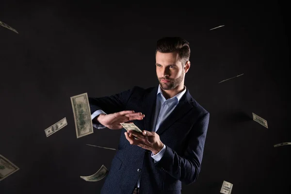 Photo of handsome business guy hold hands usa bucks rich successful millionaire throwing banknotes spend money on girlfriend wear blue costume blazer shirt isolated black color background — Stock Photo, Image