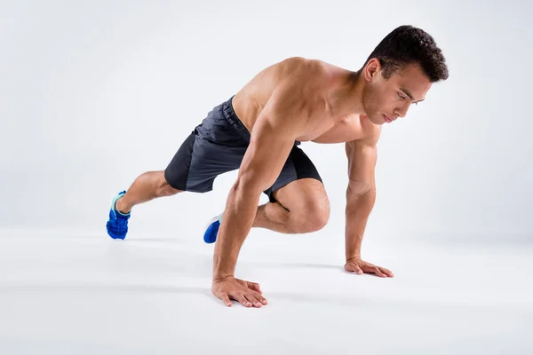 Foto de perfil de cuerpo completo de deportista guapo de piel oscura chico de pie en las manos posición de la tabla cambiando las piernas haciendo escalador de montaña ejercicio pantalones cortos zapatillas aisladas de color blanco fondo — Foto de Stock