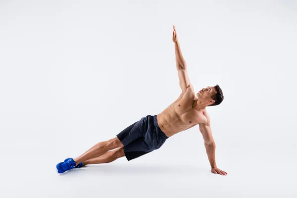 Full length photo of handsome macho sportsman dark skin guy naked chest warming up exercise focused stand plank on one arm body sculpt wear shorts sneakers isolated white color background — Stock Photo, Image