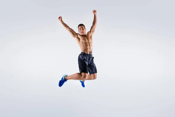 フルサイズ写真のハンサムなスポーツマンダークスキン男裸胸ジャンプ高アップお祝い競争受賞腕を上げますショートパンツ孤立ホワイトカラーの背景を着用 — ストック写真