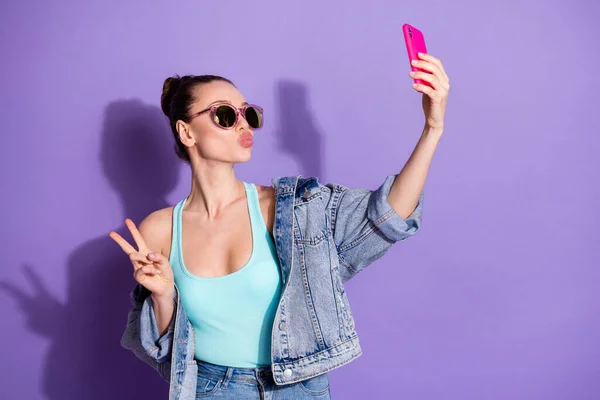 Retrato de chica encantadora blogger uso smartphone hacer selfie v-signo enviar aire beso seguidores suscriptores usar vaqueros chaqueta singlet aislado sobre violeta color fondo —  Fotos de Stock