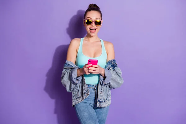 Portrait of surprised shocked girl use cellphone blogging impressed social media followers subscribers wear denim streetstyle tank top isolated over violet color background — Stock Photo, Image
