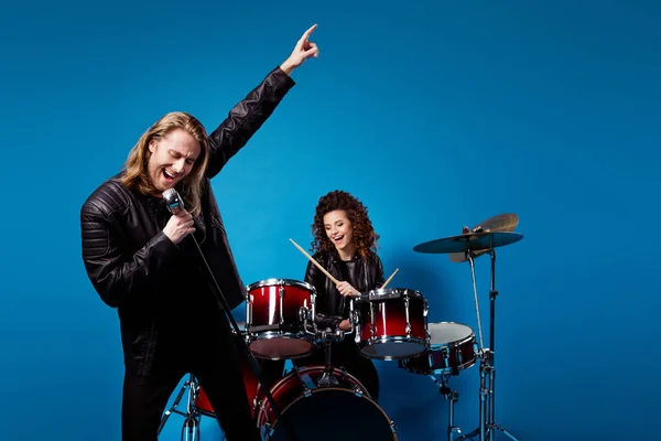 Portrait of crazy funky popular rock band two people man sing mic composition woman play drum drumstick enjoy punk festival night club tour isolated over blue color background
