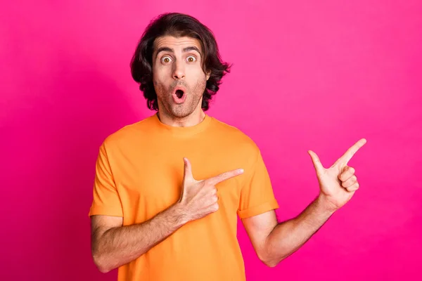 Foto de joven barbudo chico indican dedos espacio vacío expresión impactada desgaste naranja camiseta aislado color rosa fondo — Foto de Stock