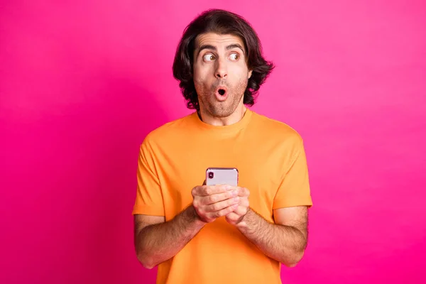 若い男の写真を保持電話見て側空のスペースは、オレンジのTシャツ孤立ピンク色の背景を着用 — ストック写真