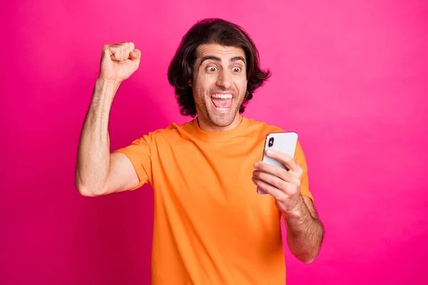 Delikanlının fotoğrafı ağzı açık cep telefonu ekranı aç yumruğunu kaldır turuncu tişört giy pembe arka plan — Stok fotoğraf