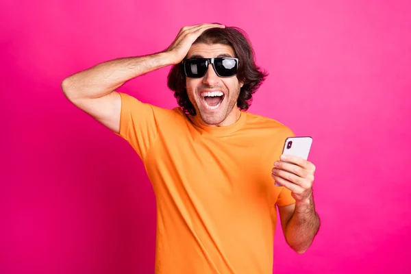 Фото чоловіка рука голови тримає телефон відкритим ротом одяг помаранчевої футболки сонцезахисний крем ізольований рожевий колір фону — стокове фото
