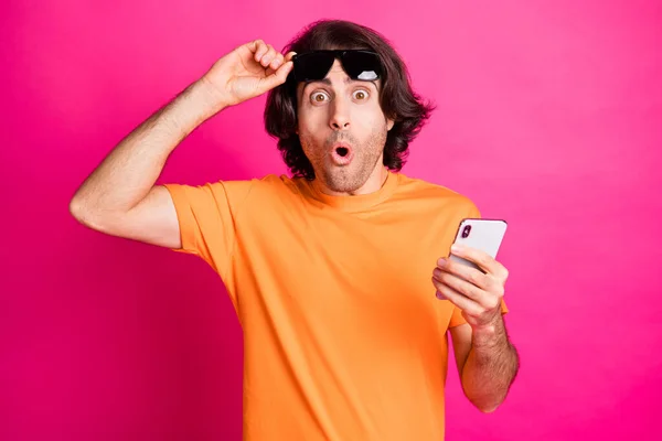 Фото молодої людини рука знімає окуляри тримайте телефонний одяг помаранчевої футболки сонцезахисний окуляри ізольований рожевий колір фону — стокове фото