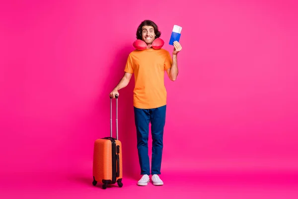 Foto de comprimento total do jovem segurar caso bilhetes passaporte desgaste pescoço almofada laranja t-shirt jeans tênis isolado cor-de-rosa fundo — Fotografia de Stock