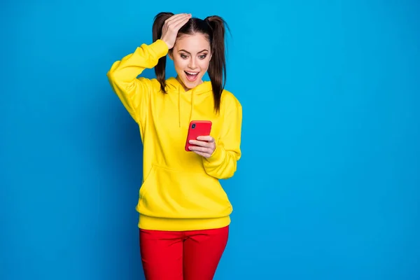 Фото смешной шокированной леди два хвоста держать телефон популярный блоггер читать пост блога положительные комментарии чрезмерно радостный износ случайный желтый капюшон красные брюки изолированы ярко-синий цвет фона — стоковое фото