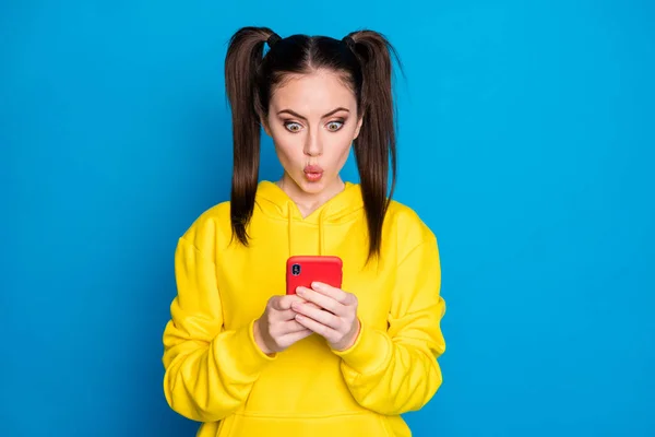 꽤 충격을 받은 여성 2 명의 꼬리 사진들이 전화기를 들고 새로운 포스트 블로그 댓글들을 읽고 있다. 이 댓글들은 평범 한 노란색 후드를 쓰고 밝은 파란색 배경을 갖고 있다. — 스톡 사진