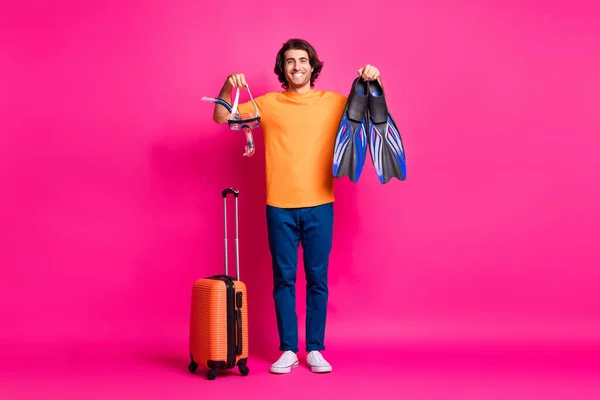 Фотографія повної довжини чоловіка в багажі тримає маску в рукаві одягають помаранчеві футболки джинси кросівки ізольовані рожевий колір фону — стокове фото